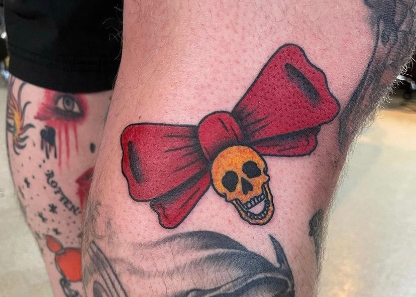 Picture, of a tattoo by Troy, tattoo artist at Top Hat Tattoo, Seattle, yellow skull with red ribbon bow