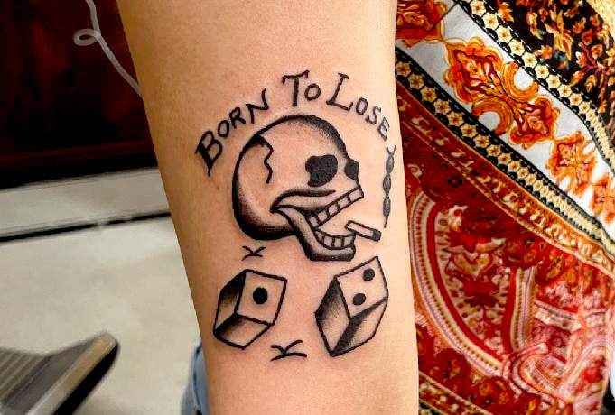 Picture, of a tattoo by Troy, tattoo artist at Top Hat Tattoo, Seattle, skull smoking a cigarette with dice and the text "Born To Lose"