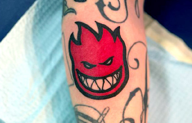 Picture, of a tattoo by Troy, tattoo artist at Top Hat Tattoo, Seattle, red flaming head cartoon with smile of fangs